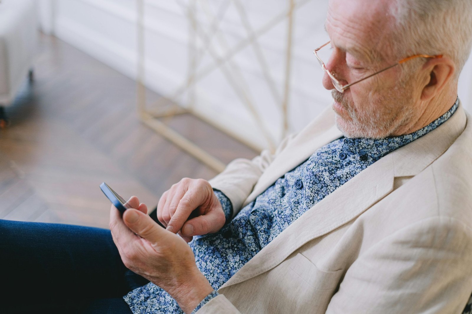 Elderly man wearing eyeglasses, using a smartphone in a bright room.
