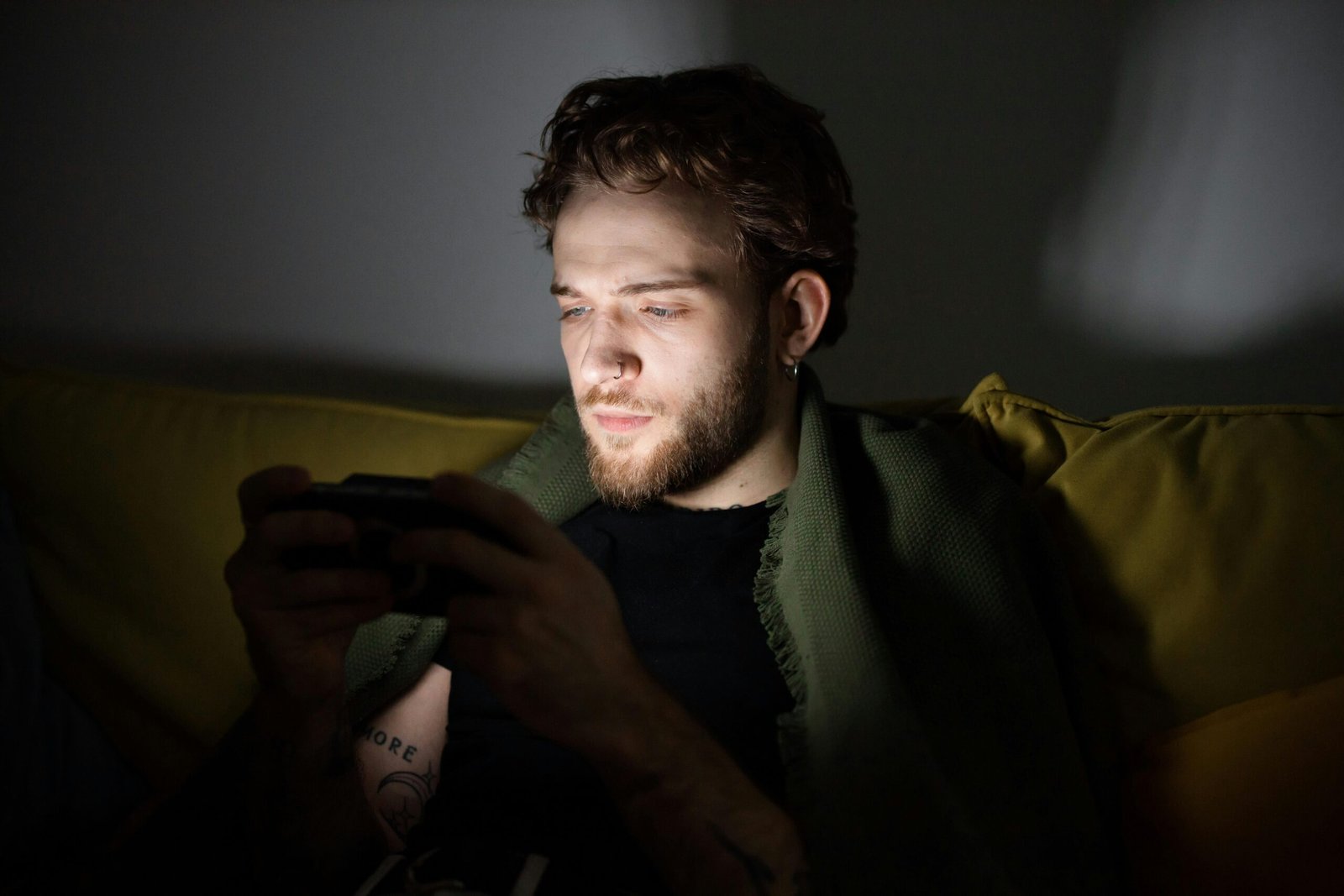 A bearded man playing video games indoors, focused on a handheld console.